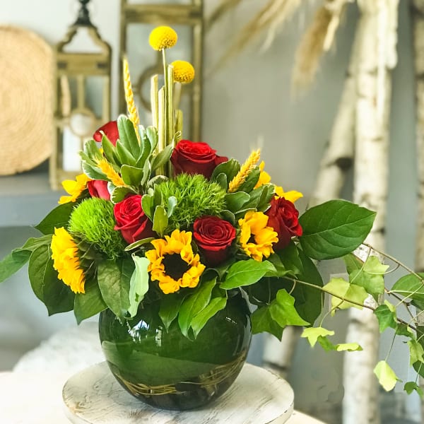 Red roses and yellow flowers arranged in a dark glass vase