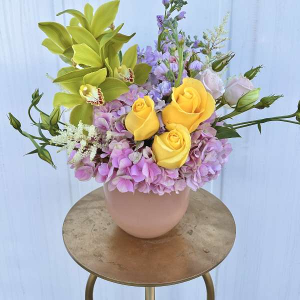 Bouquet of yellow roses, green orchids, and pink hydrangeas in a blush vase