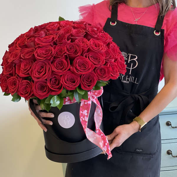 Large red rose arrangement in a black hatbox with a pink ribbon
