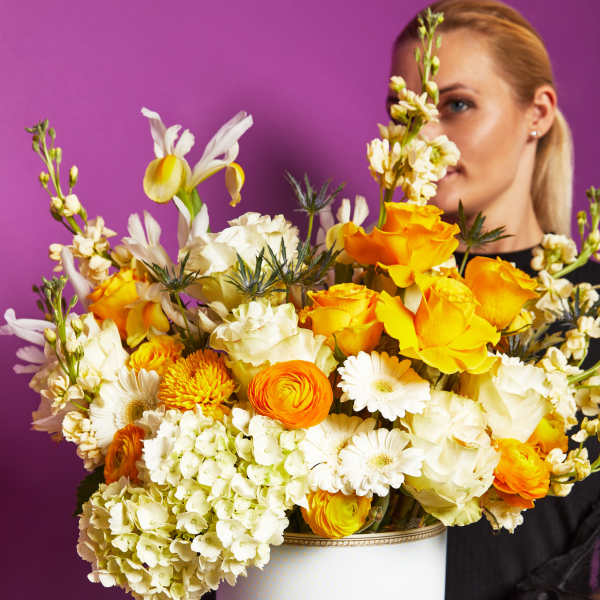 Large bouquet of yellow, white, and orange flowers in a white hatbox