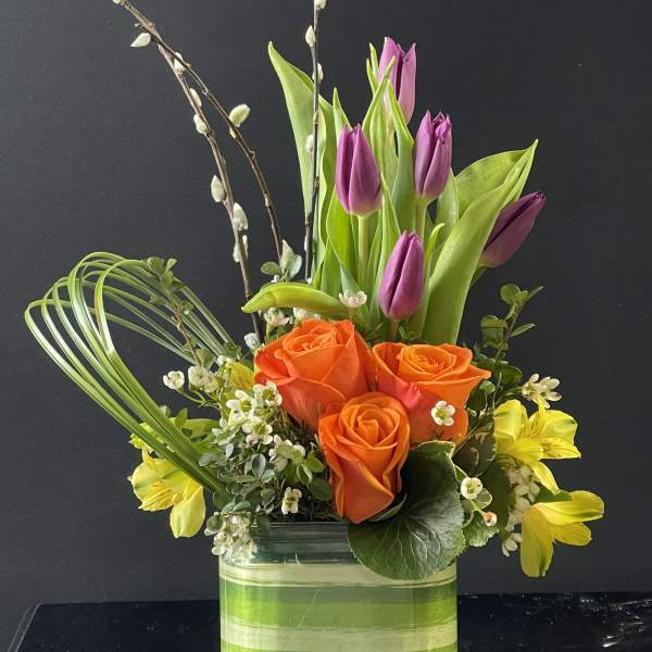 Orange roses and purple tulips in a striped glass vase
