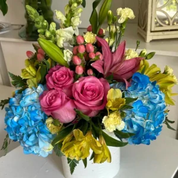 Colorful bouquet of roses, hydrangeas, and mixed blooms in a white vase