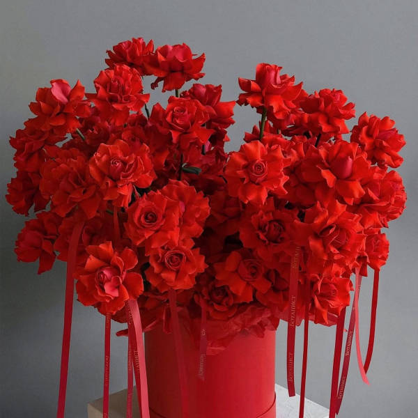 Red rose bouquet in a red cylindrical box with long ribbon tails