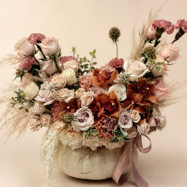 Large bouquet of blush roses, carnations, and orchids in a pale pumpkin vase