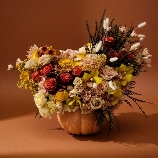 Mixed bouquet in a pumpkin-shaped vase with yellow, cream, and red flowers