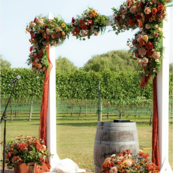 Large floral arch with orange and red flowers at an outdoor venue