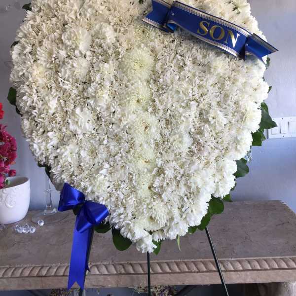 Heart-shaped white floral wreath with a blue ribbon reading SON