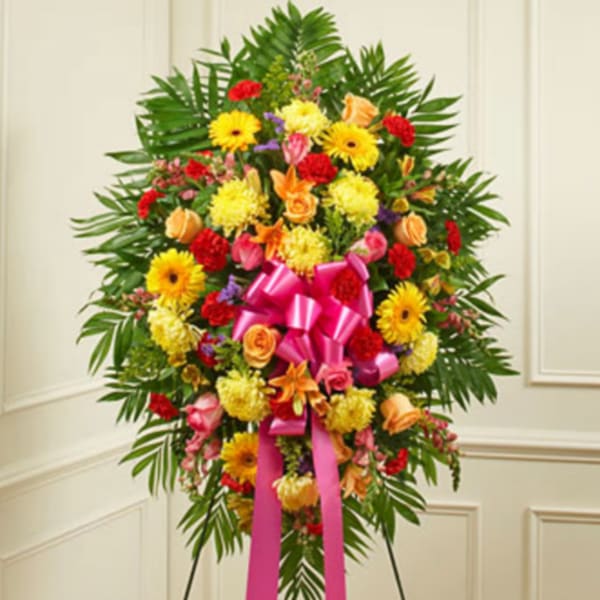 Standing floral spray with mixed bright flowers and a pink ribbon