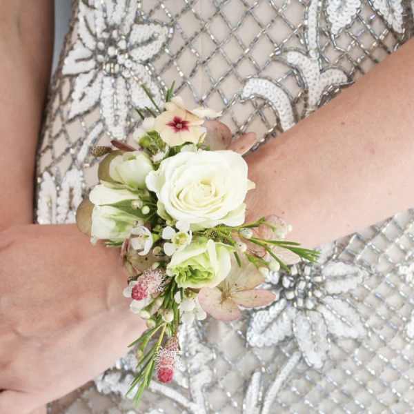 Wrist corsage of white roses and small pink flowers on a beaded dress.