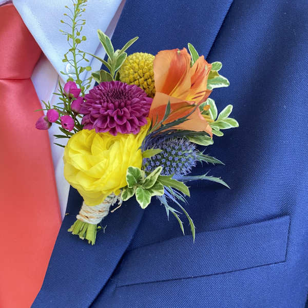 Colorful boutonniere with yellow, orange, purple and blue blooms on a navy suit jacket.
