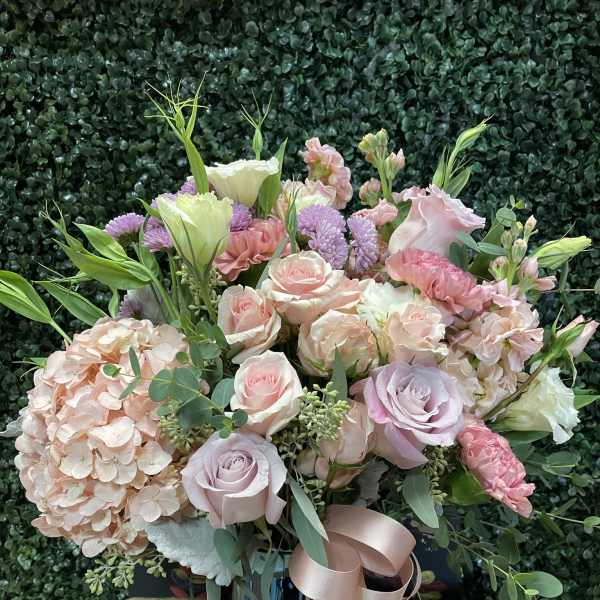 Pastel bouquet of roses, hydrangea, and lisianthus in a blue vase with ribbon