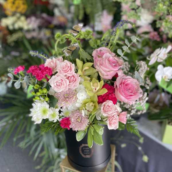 Pink roses and mixed blooms arranged in a black hatbox