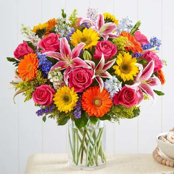Mixed bouquet of roses, lilies, and daisies in a clear glass vase