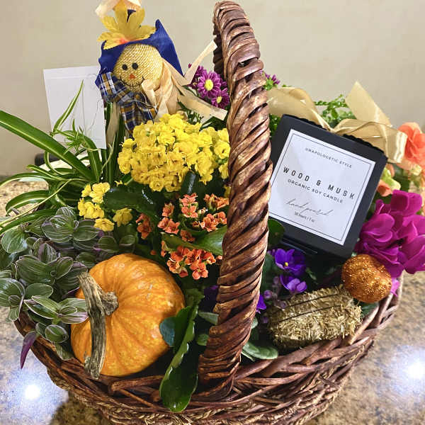 Autumn gift basket with yellow and orange flowering plants, a pumpkin, candle, and fall decorations