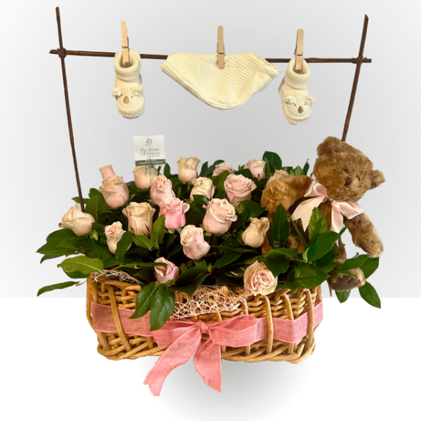 Basket of pale pink roses with a teddy bear and baby booties hanging above on a clothesline