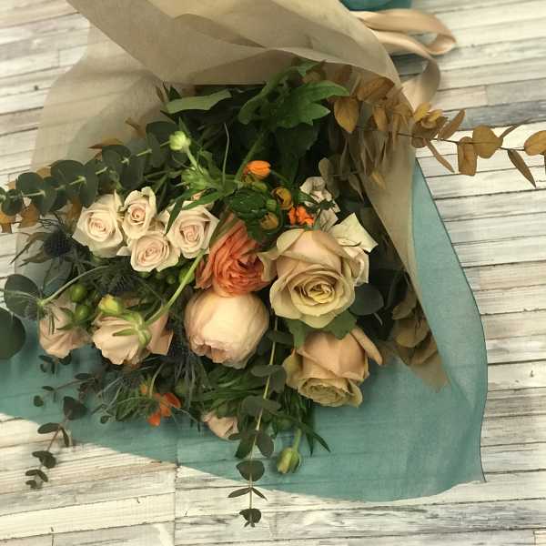 Bouquet of blush and peach roses wrapped in tan and teal paper