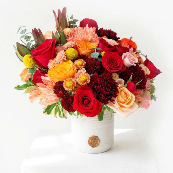 Mixed bouquet of red, peach, and yellow flowers in a white vase