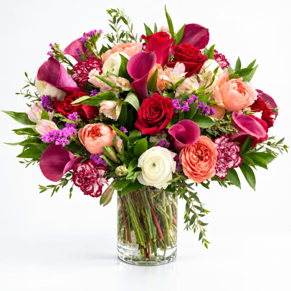 Mixed bouquet of roses, calla lilies, and ranunculus in a clear glass vase