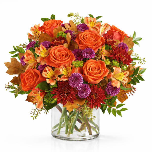 Orange roses and mixed fall flowers in a clear glass vase