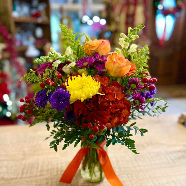 Colorful mixed bouquet in a glass vase with orange, yellow, purple, and red blooms