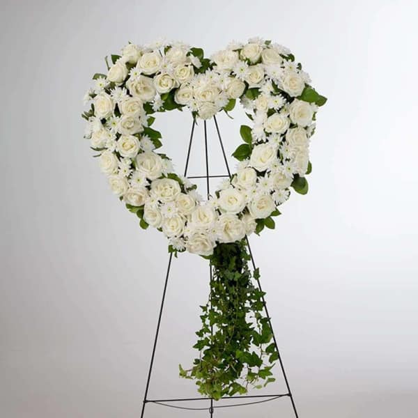 White rose heart wreath on a black easel with trailing greenery