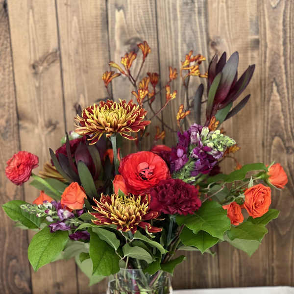 Mixed bouquet in a clear vase with orange, red, and purple blooms