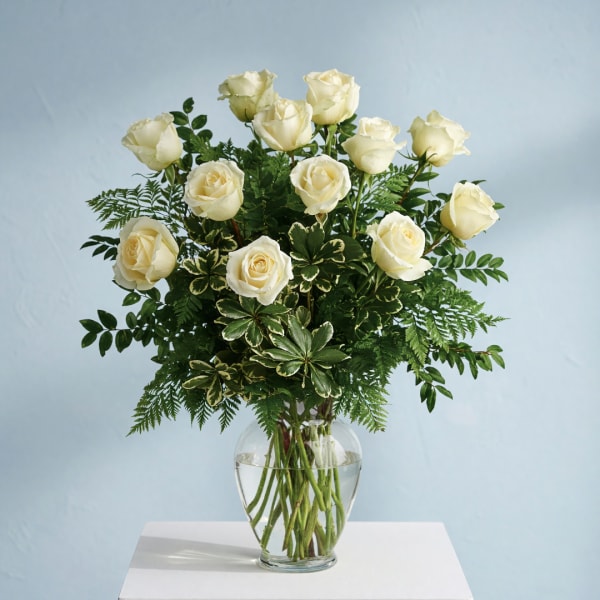 White roses in a clear glass vase with mixed greenery
