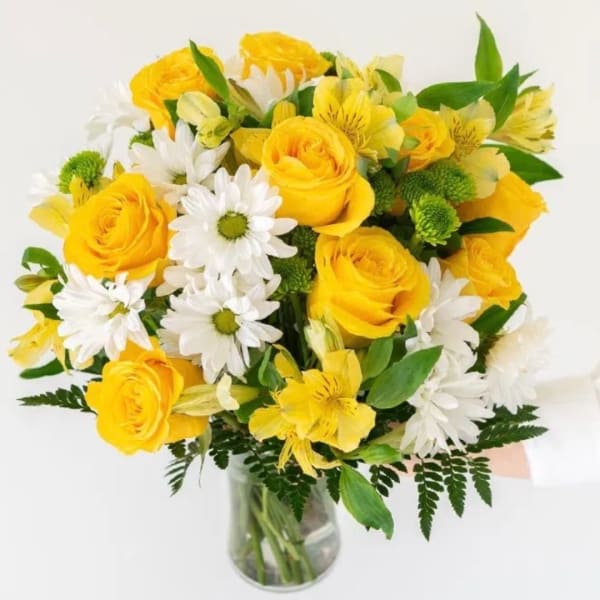 Yellow roses and white daisies in a clear glass vase