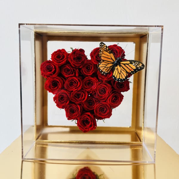 Heart-shaped red rose arrangement in a clear box with a butterfly accent