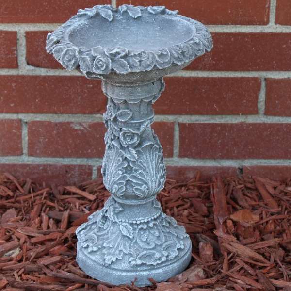 Decorative gray stone birdbath pedestal against a brick wall