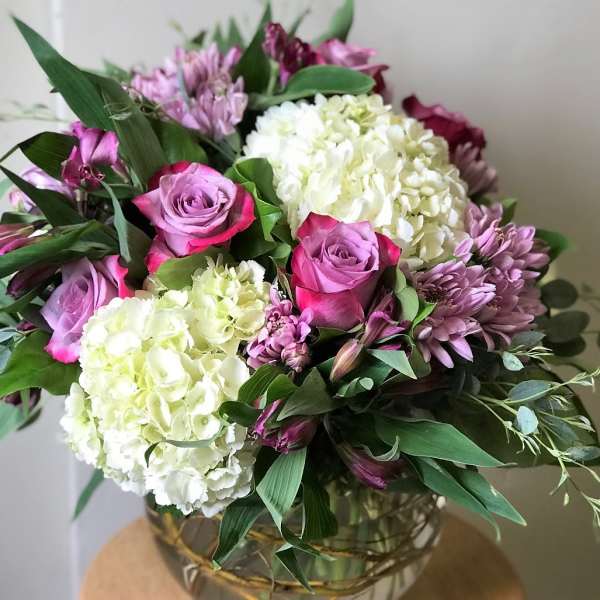 Bouquet of pink roses, white hydrangeas, and purple flowers in a glass vase