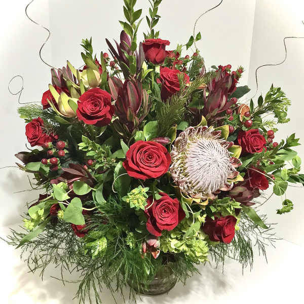 Large arrangement of red roses and king protea in a clear glass vase