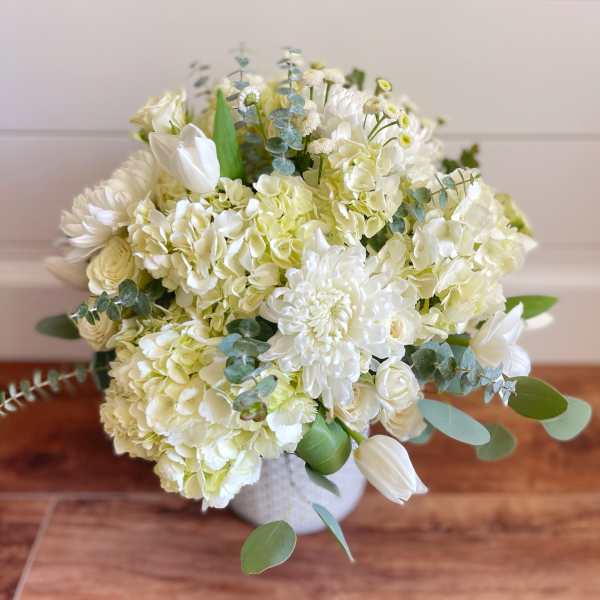 White floral bouquet with hydrangeas, tulips, and eucalyptus in a vase