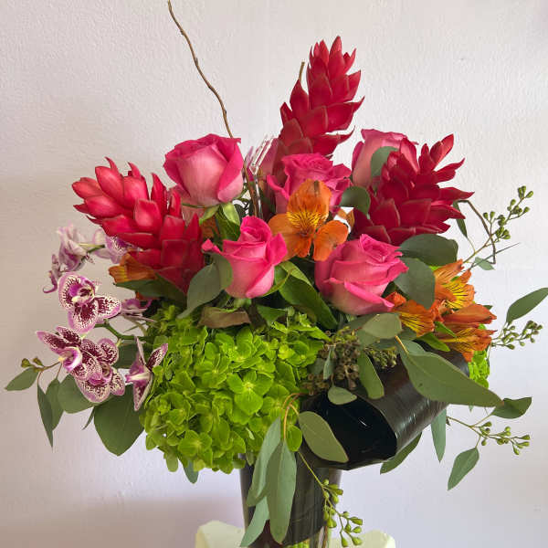 Bouquet of pink roses, red tropical blooms, and orchids in a glass vase
