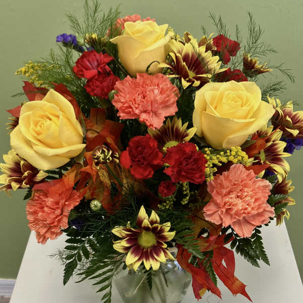 Mixed bouquet of yellow roses, carnations, and daisies in a glass vase