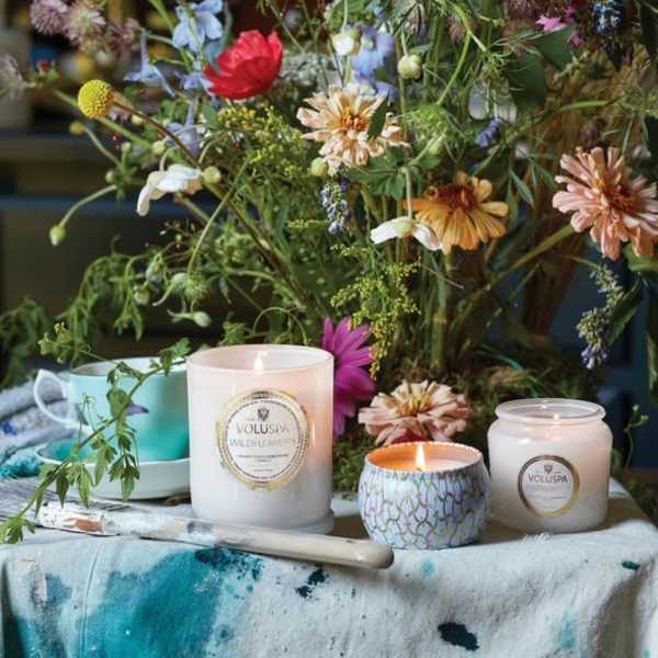 Wildflower arrangement with three lit candles and a turquoise cup on a painted cloth