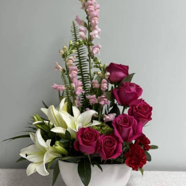 Pink roses and white lilies arranged in a white bowl vase