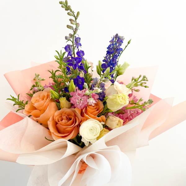 Hand-tied bouquet of orange, white, pink, and blue flowers in pastel wrapping