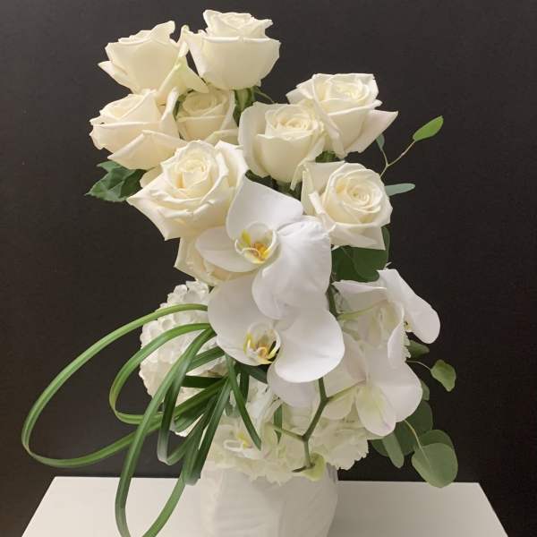 White roses and orchids arranged in a white vase