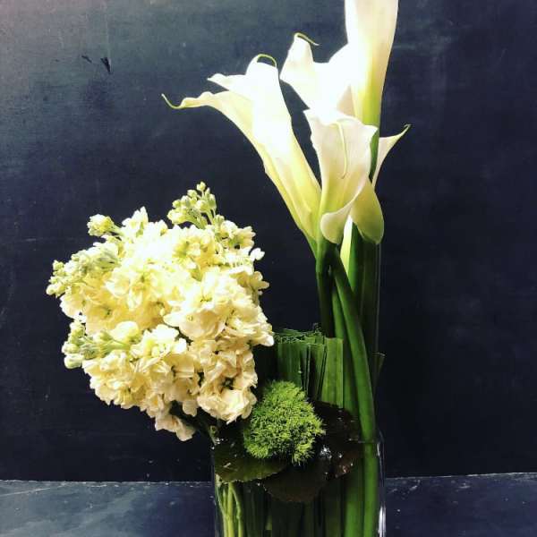 White calla lilies and pale yellow flowers in a glass vase