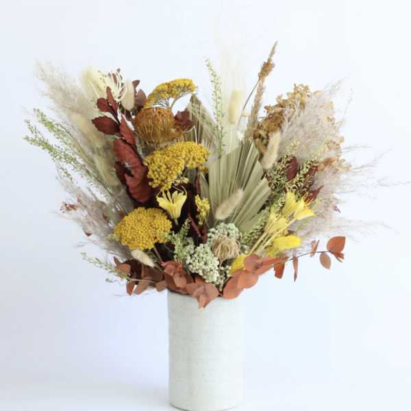 Tall dried-style arrangement with yellow and rust flowers in a white cylindrical vase