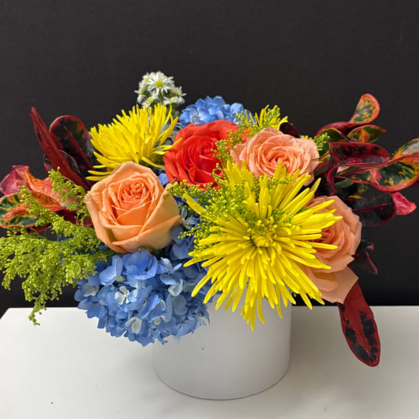 Colorful bouquet of roses, hydrangeas, and yellow mums in a white vase