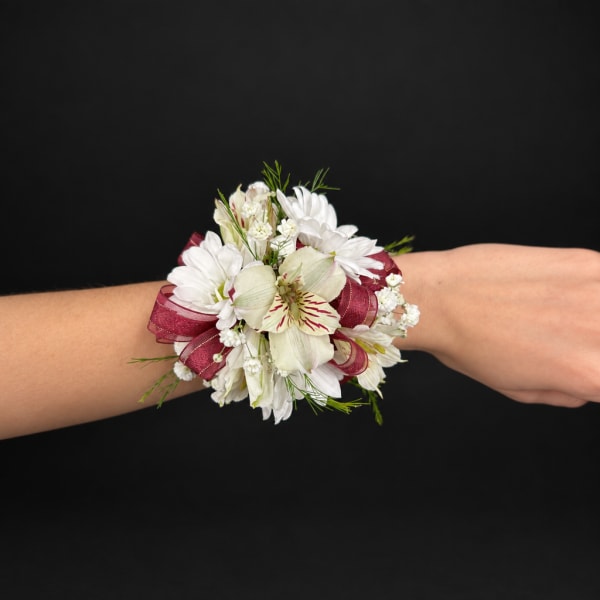 White floral wrist corsage with burgundy ribbon on a person's wrist