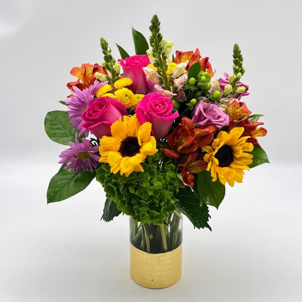 Mixed bouquet with pink roses, sunflowers, and purple blooms in a glass vase