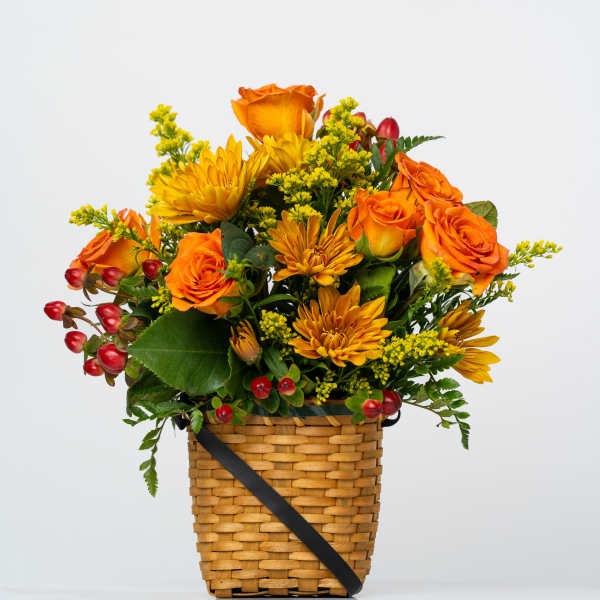 Orange roses and yellow mums in a woven basket with red berries