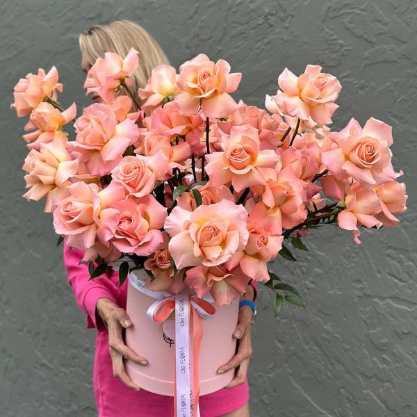 Pink roses arranged in a round hatbox with a ribbon bow