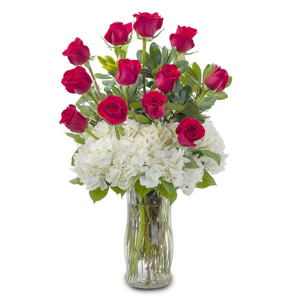 Red roses arranged with white hydrangeas in a clear glass vase