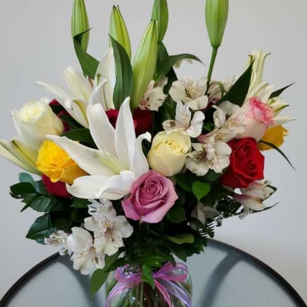 Mixed bouquet of roses and lilies in a glass vase with a ribbon