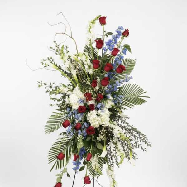 Tall standing floral spray with red roses, white blooms, and blue flowers