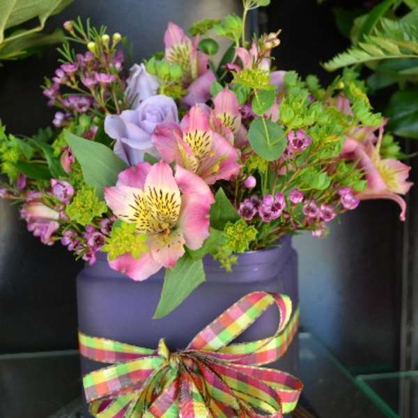 Pink and lavender flowers in a purple container with a plaid ribbon